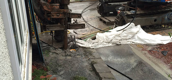 Job site during geothermal drilling, rig in place near the foundation, protected by a tarp
