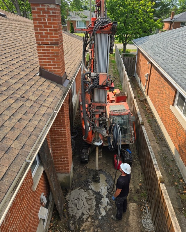 Drill rig set up between the fence and the building during geothermal drilling.